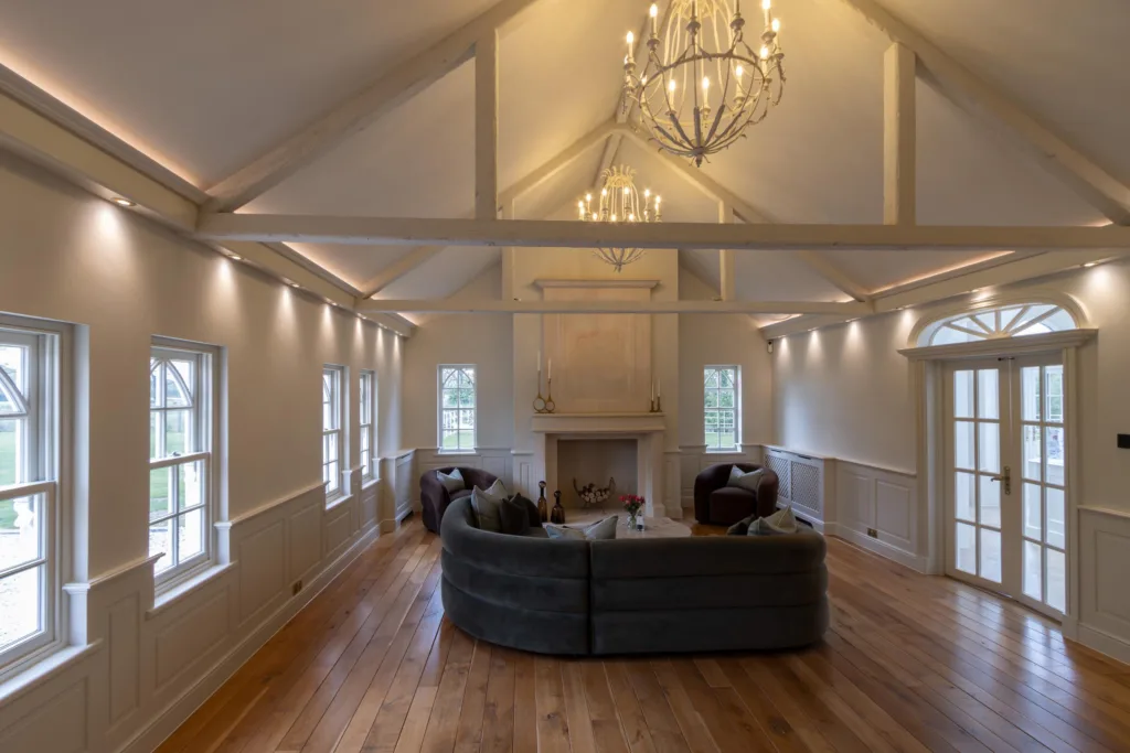 Large open-plan living space with a vaulted beamed ceiling, chandeliers, panelled walls and a central fireplace