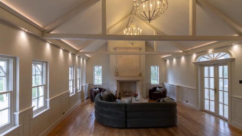 Large open-plan living space with a vaulted beamed ceiling, chandeliers, panelled walls and a central fireplace