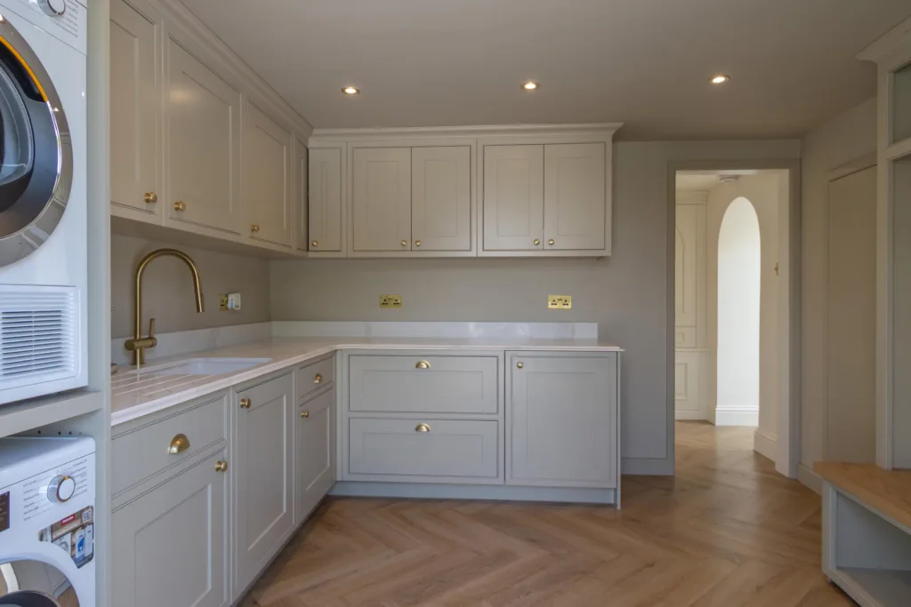 Fitted utility room with cream shaker cabinetry, a stacked washing machine and tumble dryer and a brushed brass tap