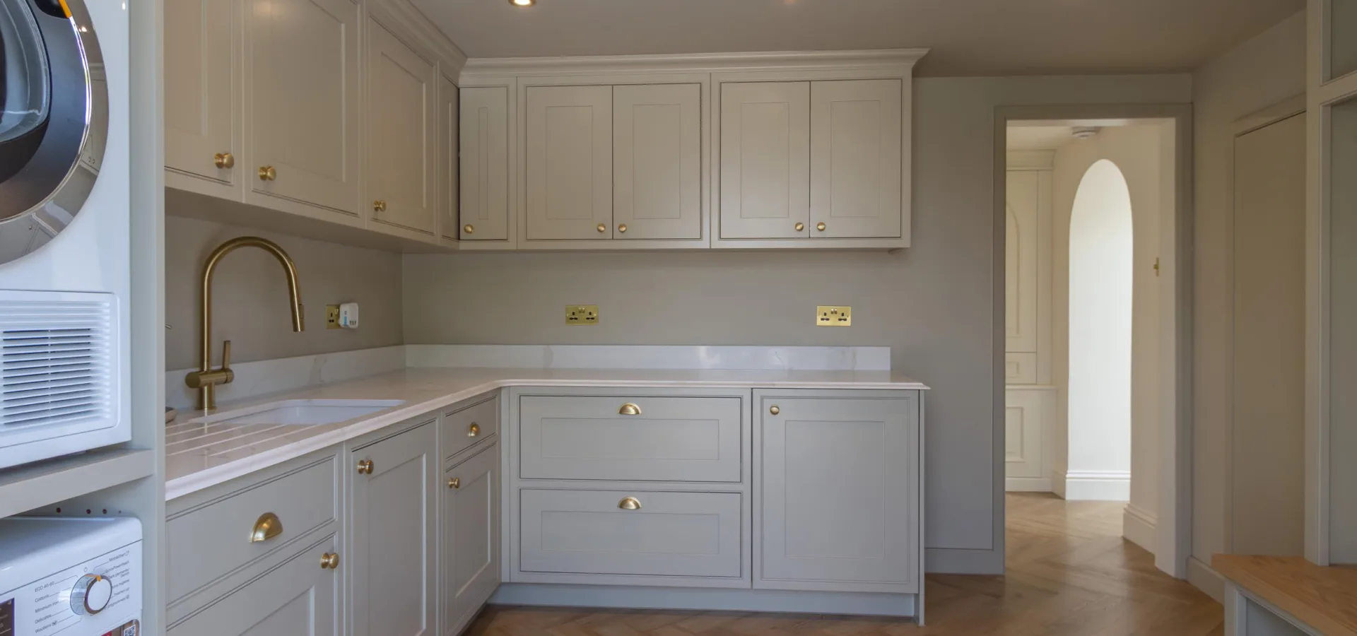 Fitted utility room with cream shaker cabinetry, a stacked washing machine and tumble dryer and a brushed brass tap