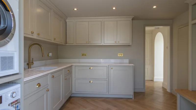 Fitted utility room with cream shaker cabinetry, a stacked washing machine and tumble dryer and a brushed brass tap