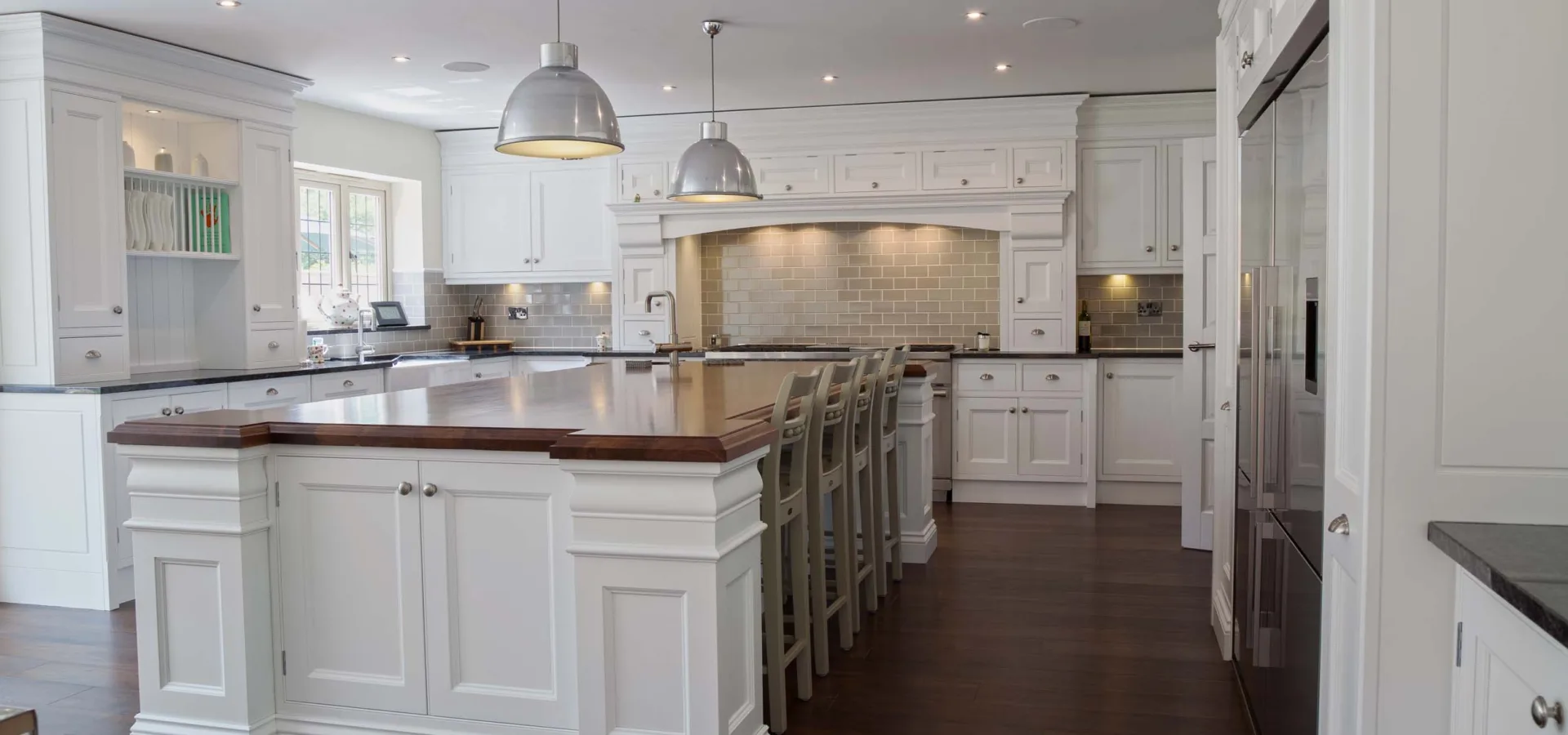 Large classic white kitchen with a long central island, pendant lighting and a dark timber floor