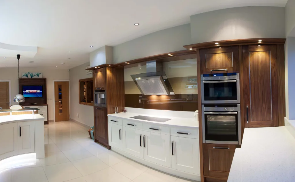 Bespoke kitchen combining cream painted cabinetry with a curved walnut island and built-in ovens