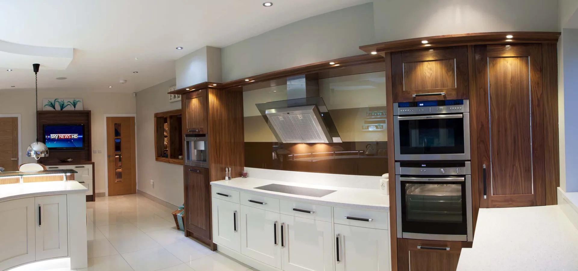Bespoke kitchen combining cream painted cabinetry with a curved walnut island and built-in ovens