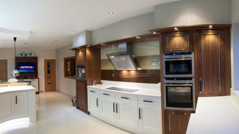 Bespoke kitchen combining cream painted cabinetry with a curved walnut island and built-in ovens